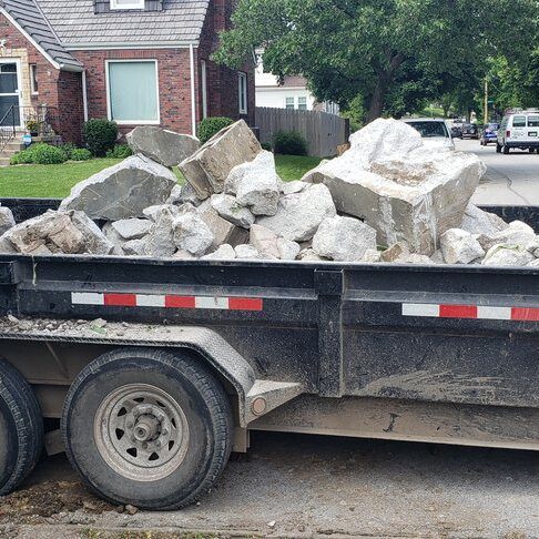 A trailer filled with large concrete rocks parked on a residential street, showcasing debris removal services.
